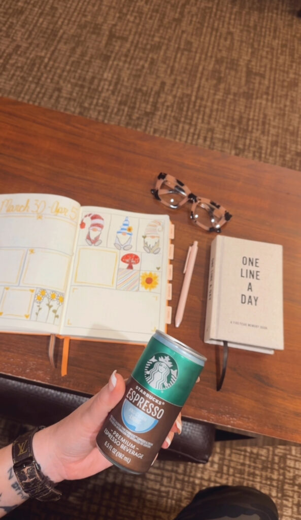 Picture of table with glasses, notebook, journal, and pen on it with someone holding a coffee drink for small business owners quarterly planning retreat